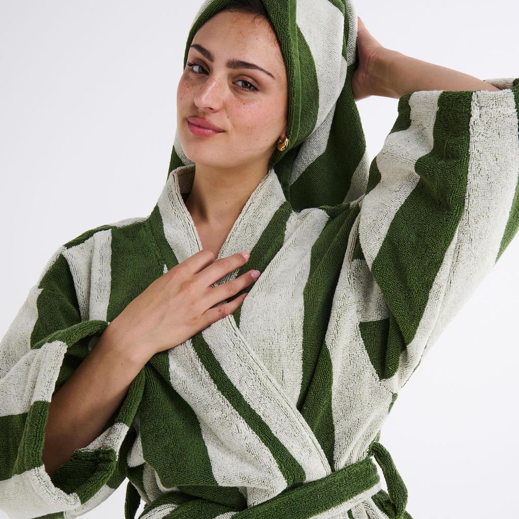 The image is of a bathrobe made from terry cloth material. The robe features a striped pattern with various shades of green, resembling moss. It has a classic design with a shawl collar, long sleeves, and a belt for tying around the waist. The texture appears soft and plush, typical of terry cloth, which is known for its absorbency and comfort. The robe is displayed against a plain background, highlighting its design and color scheme.