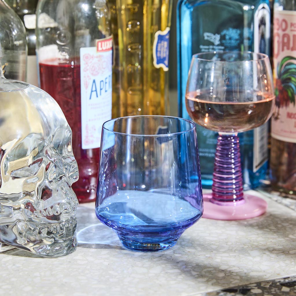 The image shows a set of two wine glasses from Kip & Co, known as the Sardinia Stalk Wine Glass 2P Set. The glasses are elegantly designed with a unique, artistic flair. They feature a clear bowl for holding the wine, which is supported by a distinctive, colorful stem that adds a touch of vibrancy and style. The stems are likely crafted to resemble a stalk, giving the glasses a modern and sophisticated appearance. The background is plain, ensuring that the focus remains on the wine glasses themselves.