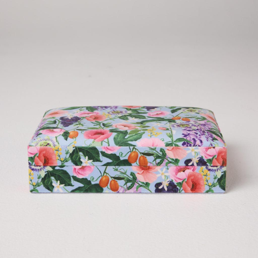 The image is of a small, velvet jewelry box from Kip & Co. It is designed in a vibrant, spring-inspired color palette, featuring a mix of pastel and bold hues. The box has a soft, plush texture typical of velvet material, and it is likely adorned with intricate patterns or designs that reflect a lively, springtime theme. The box is compact, suitable for storing small pieces of jewelry like rings, earrings, or necklaces.