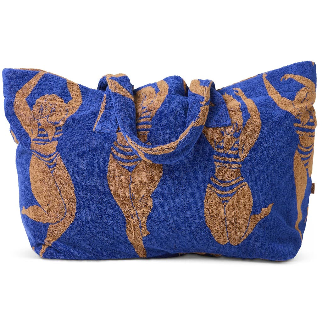 The image shows a large, colorful beach bag made from terry cloth material. The bag features a vibrant, multicolored striped pattern with shades of pink, orange, yellow, and blue, reminiscent of a sunset or a sun-kissed theme. It has sturdy handles for easy carrying and appears spacious, ideal for holding beach essentials. The overall design is cheerful and summery, perfect for a day at the beach or pool.