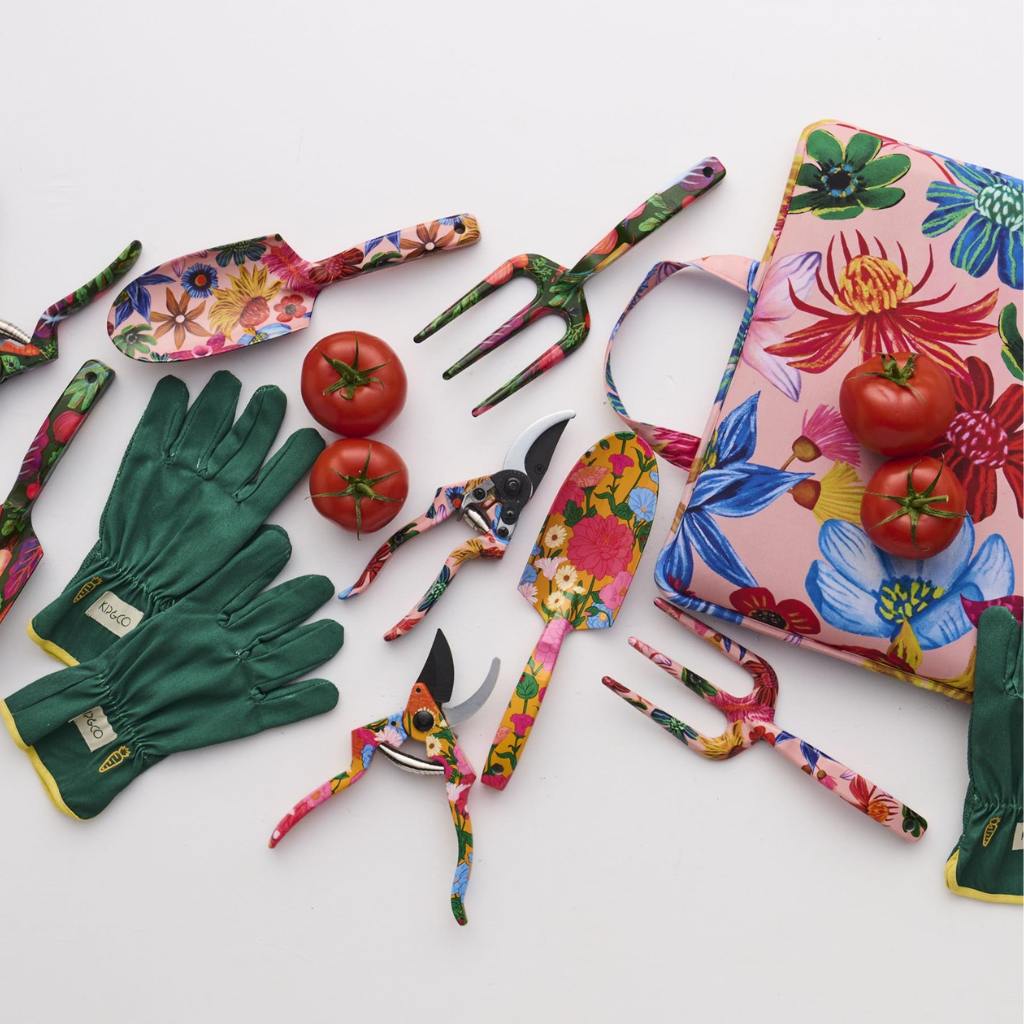The image shows a set of garden tools and gloves with a vibrant floral design. The tools include a trowel and a hand fork, both featuring handles adorned with colorful wildflower patterns. The gloves are similarly decorated, matching the floral theme of the tools. The background is a neutral color, allowing the bright and cheerful design of the garden set to stand out. This set is likely intended for gardening enthusiasts who appreciate both functionality and aesthetic appeal in their gardening accessories.