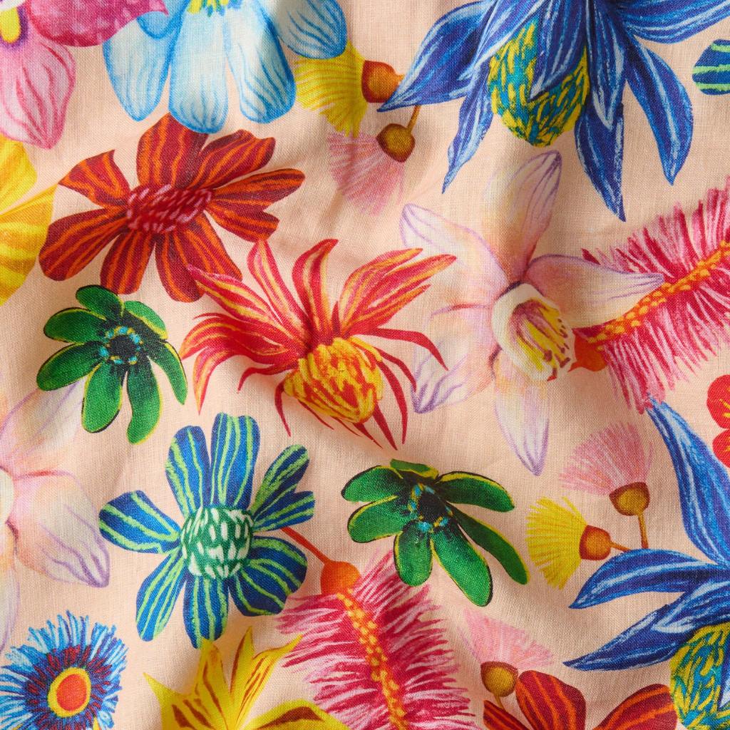 The image is of a colorful tea towel featuring a vibrant floral design. The pattern includes a variety of wildflowers in full bloom, showcasing an array of colors such as pink, yellow, blue, and green. The flowers are intricately detailed, giving the towel a lively and cheerful appearance. The background is a soft, neutral color that allows the bright flowers to stand out. The overall look is fresh and inviting, perfect for adding a touch of nature-inspired beauty to a kitchen setting.