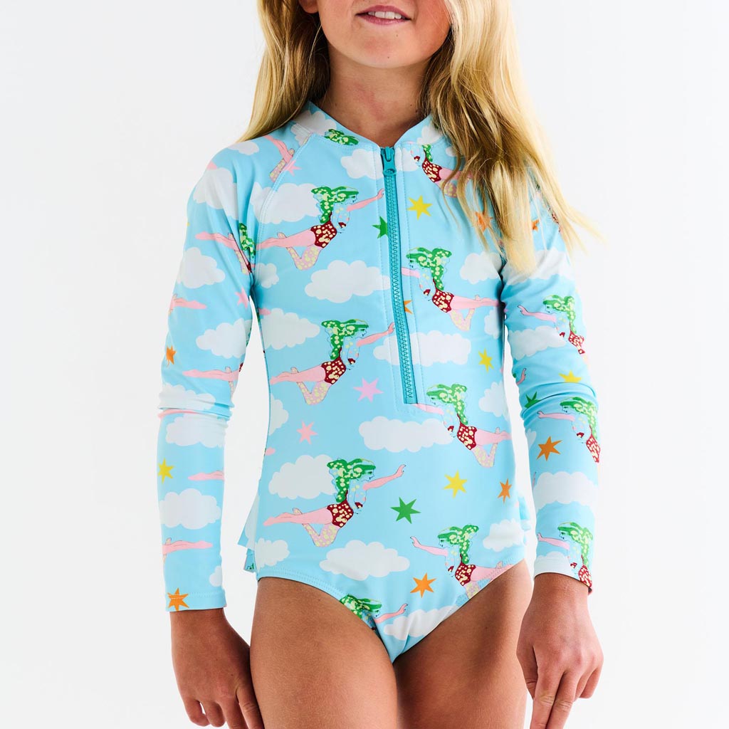 The image is of a long-sleeve bathing suit designed by Kip & Co in collaboration with The Beatles. The design is inspired by the song "Lucy In The Sky With Diamonds." The bathing suit features a vibrant and colorful pattern, likely incorporating psychedelic elements and motifs reminiscent of the 1960s era, reflecting the song's whimsical and imaginative themes. The colors are bright and eye-catching, possibly including shades of pink, blue, yellow, and green, with abstract shapes or illustrations that evoke