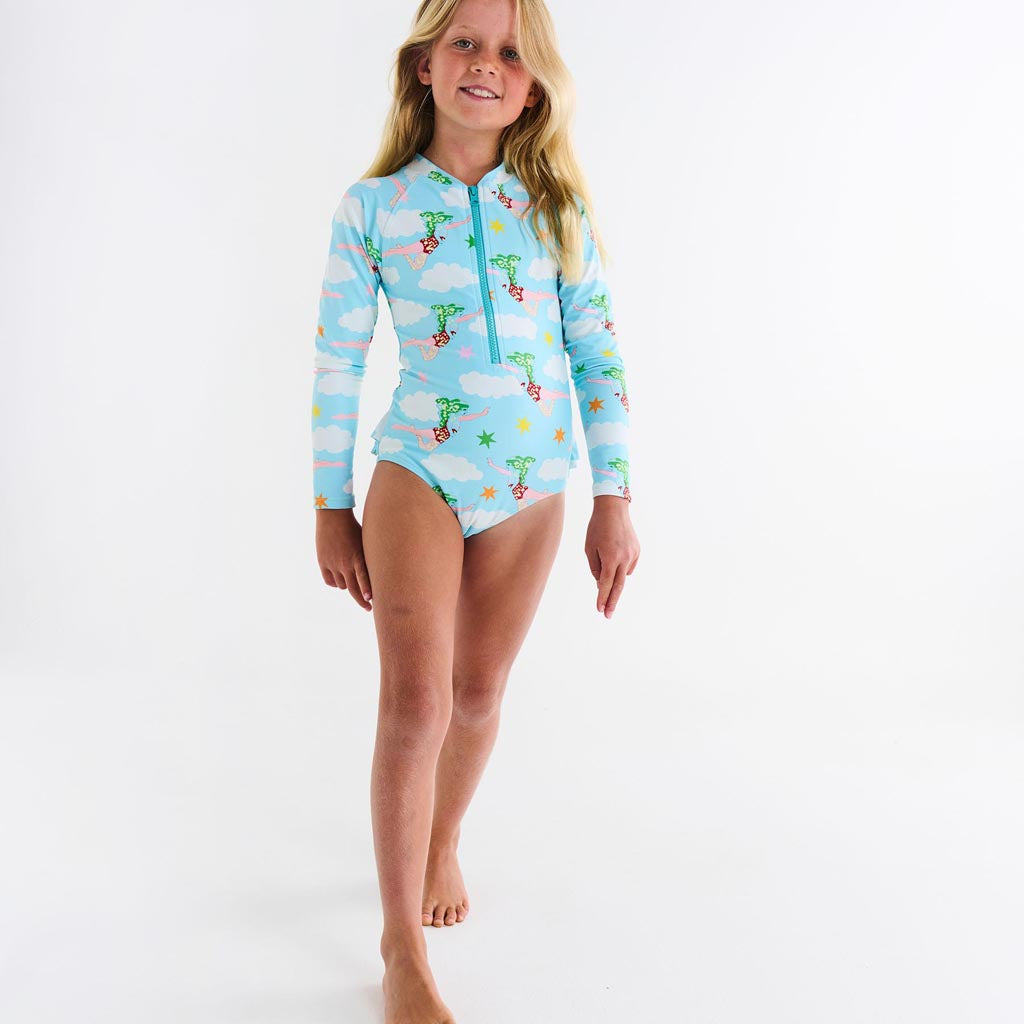 The image shows a long-sleeve bathing suit designed in collaboration between Kip & Co and The Beatles. The design is inspired by the song "Lucy In The Sky With Diamonds." The bathing suit features a vibrant and colorful pattern with psychedelic elements, likely incorporating imagery such as stars, diamonds, and abstract shapes, reflecting the whimsical and surreal nature of the song. The background is likely a solid color to highlight the intricate design of the bathing suit.