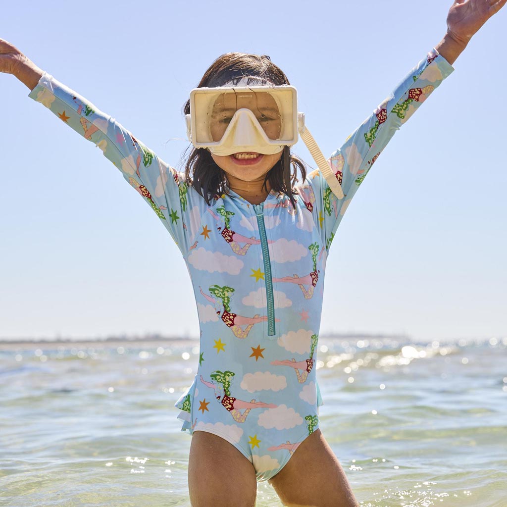 The image is of a long-sleeve bathing suit designed by Kip & Co in collaboration with The Beatles. The design is inspired by the song "Lucy In The Sky With Diamonds." The bathing suit features vibrant, psychedelic patterns and colors reminiscent of the 1960s, with abstract shapes and possibly floral or star-like motifs. The overall aesthetic is colorful and whimsical, capturing the essence of the iconic song.