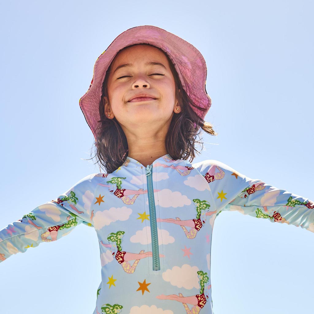 The image is of a long-sleeve bathing suit designed in collaboration between Kip & Co and The Beatles. The design is inspired by the song "Lucy In The Sky With Diamonds." The bathing suit features vibrant, psychedelic patterns and colors reminiscent of the 1960s, with abstract and whimsical elements that capture the essence of the song's imaginative and dreamlike quality. The overall look is colorful and eye-catching, suitable for someone who appreciates both fashion and music history.