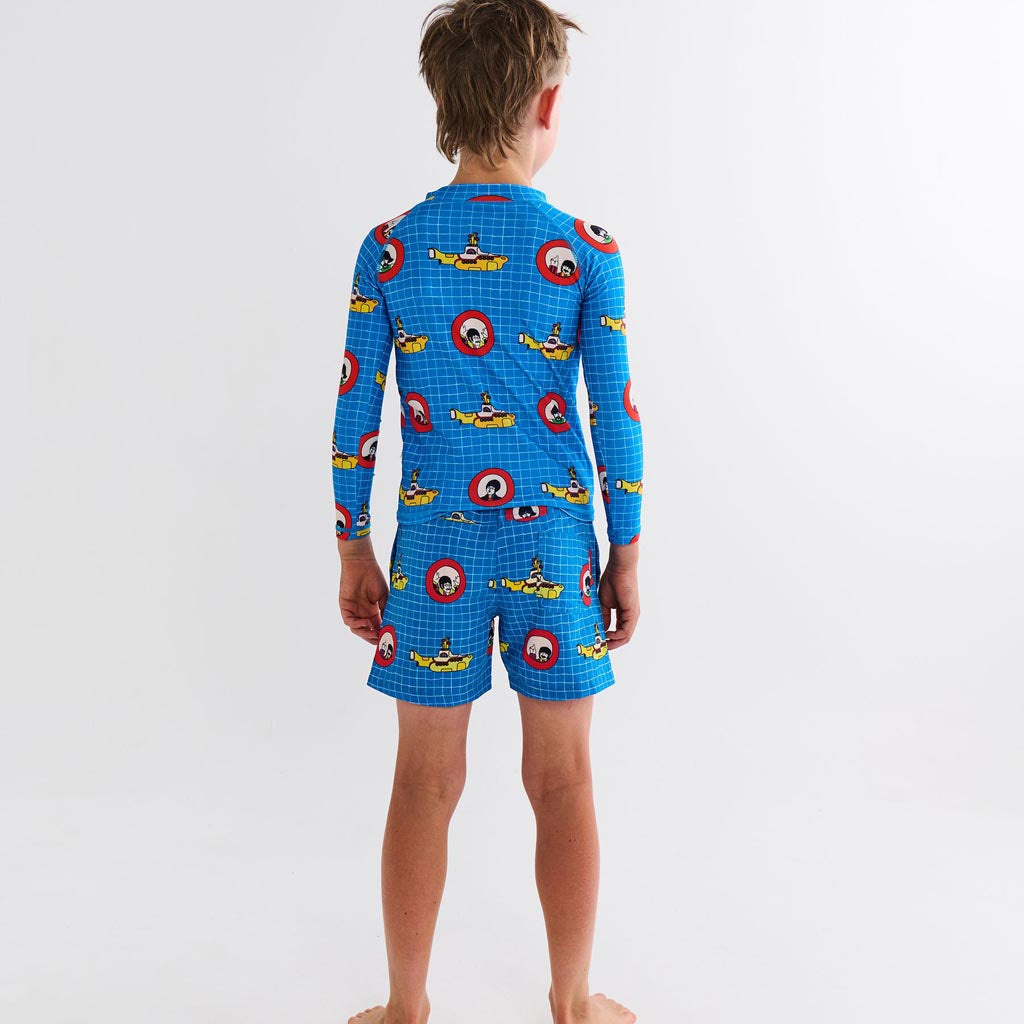 The image is likely a promotional photo for a collaboration between Kip & Co and The Beatles, featuring clothing items inspired by the iconic "Yellow Submarine" theme. The image may show colorful board shorts (boardies) and a rash vest, both adorned with vibrant, psychedelic designs reminiscent of the artwork from The Beatles' "Yellow Submarine" era. The clothing items are likely displayed against a plain or minimal background to highlight their unique patterns and colors.