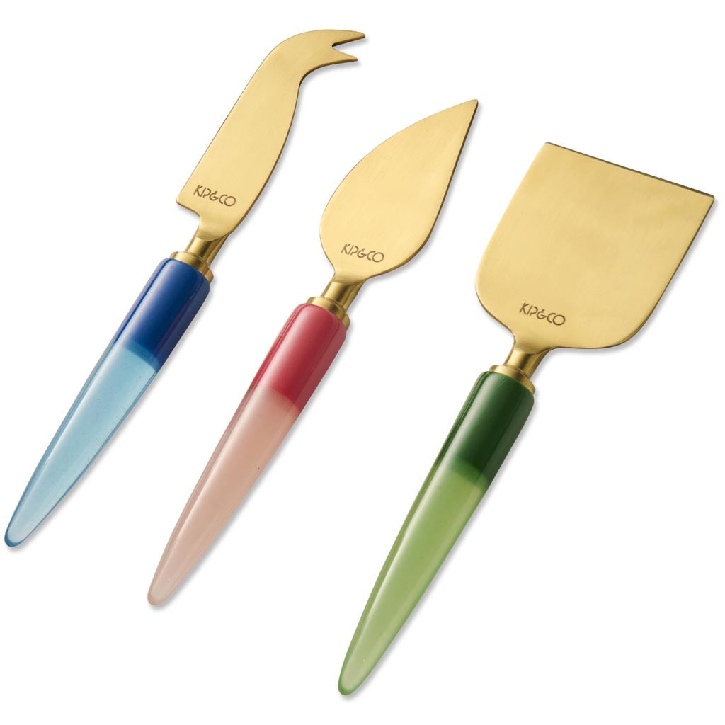 The image shows a set of three cheese knives, each with a unique and colorful handle design. The handles are adorned with vibrant, jewel-like embellishments, giving them a luxurious and artistic appearance. The blades of the knives are metallic and have a sleek, polished finish. The knives are arranged side by side on a plain, neutral background, highlighting their intricate and eye-catching designs.