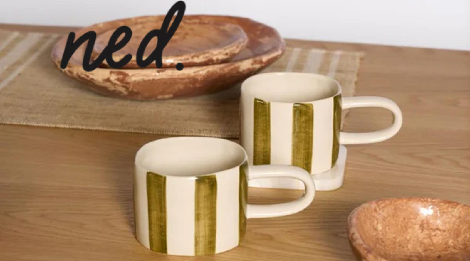 Two ceramic mugs with green stripes on a wooden surface, with 'ned.' branding.