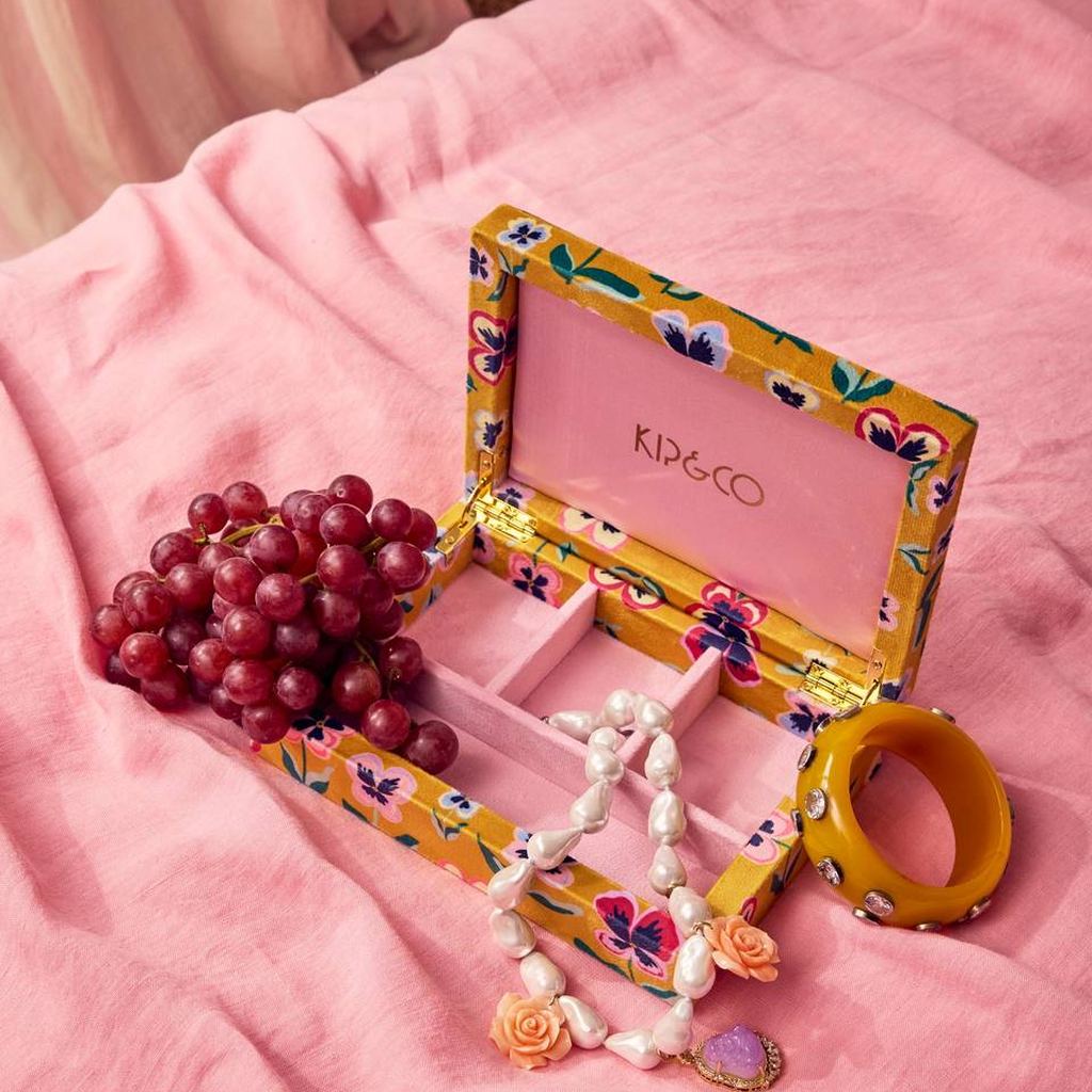 Pretty Pansy jewellery box open on pink linen with necklaces and grapes