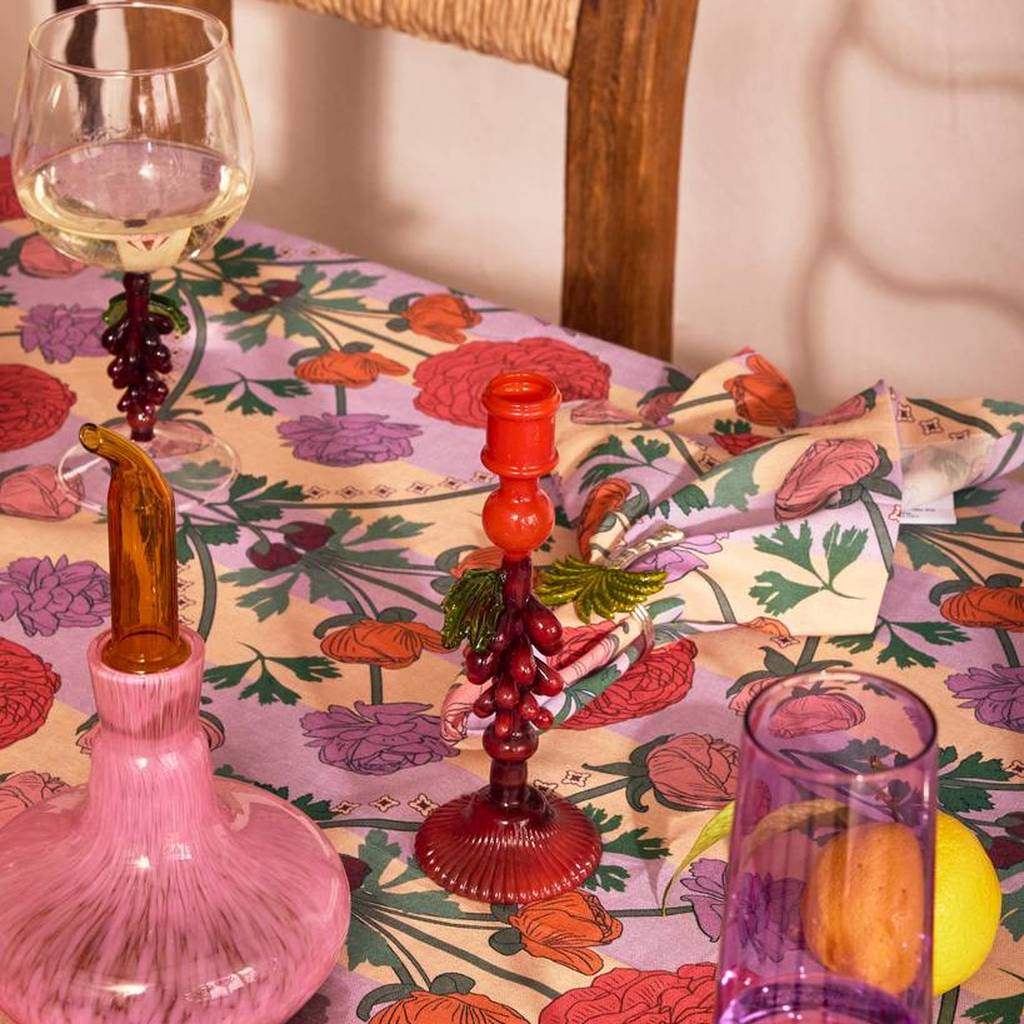 Red Under The Vine candlestick on a floral tablecloth beside a pink decanter