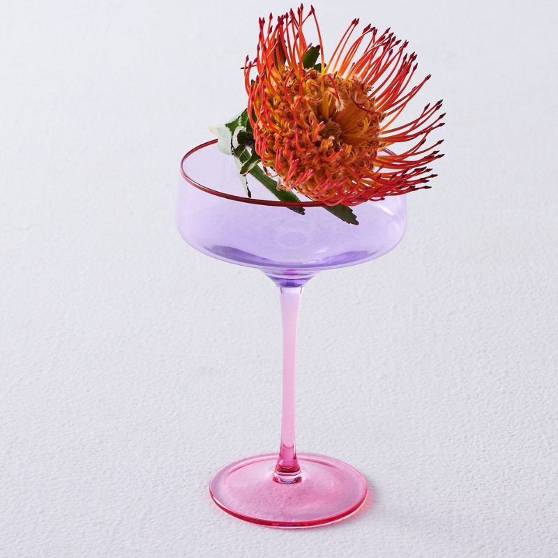The image likely features a set of elegant lilac-colored margarita glasses from Kip &amp; Co, available exclusively at Cove. The glasses are stylishly designed, perfect for adding a touch of sophistication to any gathering or celebration.