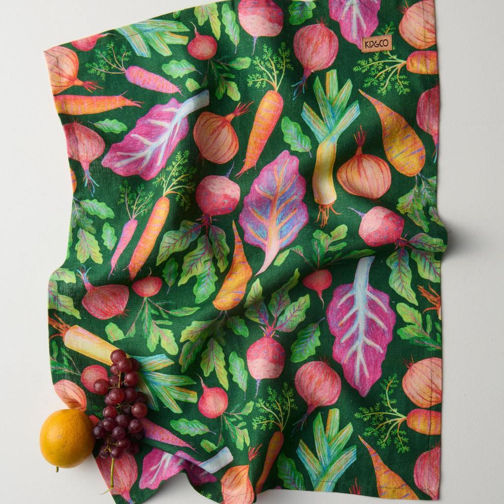 The image is of a tea towel featuring a colorful and artistic design of a veggie soup recipe. The towel likely displays various vegetables and ingredients, along with instructions or steps to make the soup. The design is both functional and decorative, making it a useful kitchen accessory.
