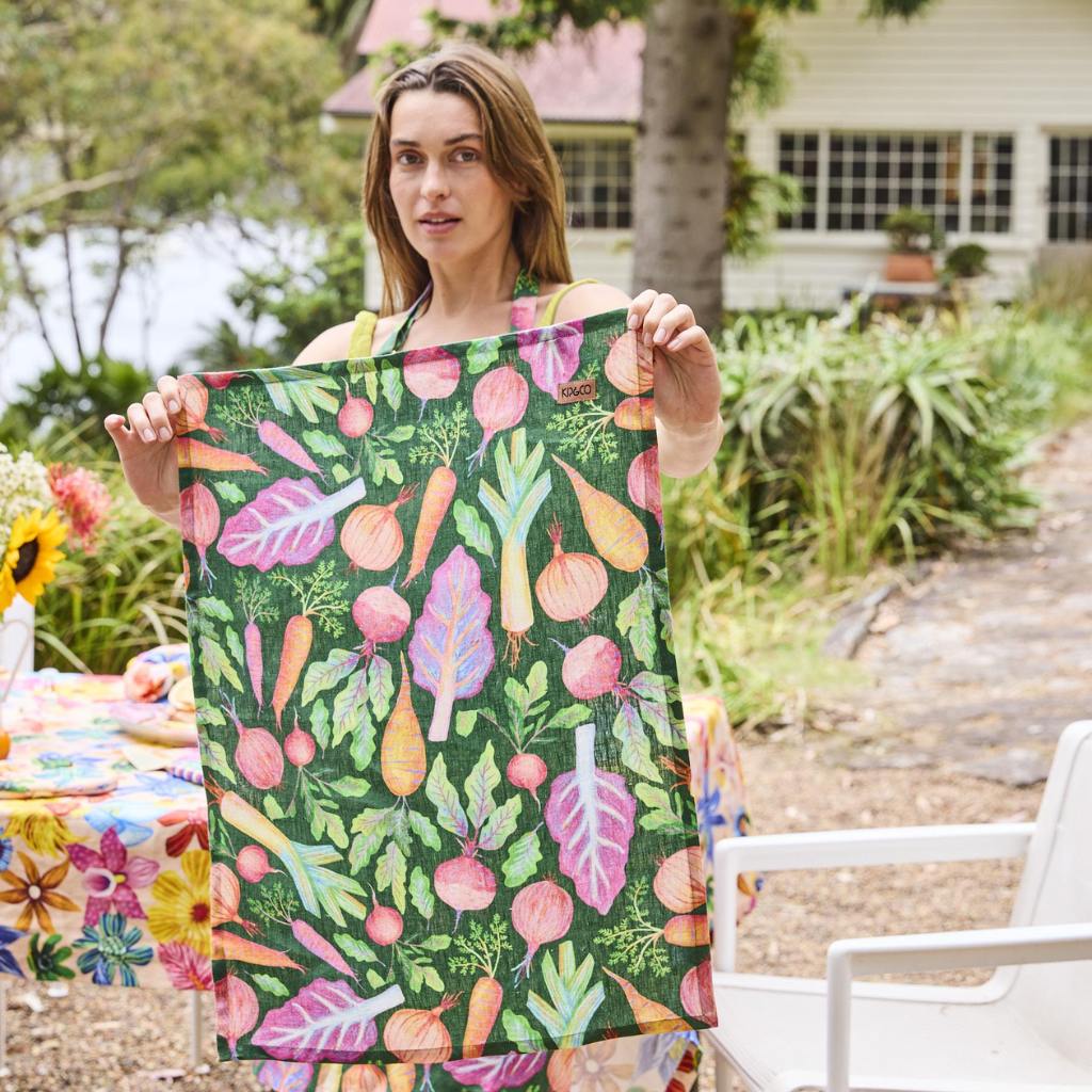The image is of a tea towel featuring a colorful and artistic design of a veggie soup recipe. The towel likely displays various vegetables and ingredients commonly used in making vegetable soup, such as carrots, tomatoes, onions, and herbs, arranged in an appealing and illustrative manner. The design may also include text with the recipe instructions or ingredient list, all set against a light or neutral background to enhance readability and visual appeal. The overall look is both functional and decorative,