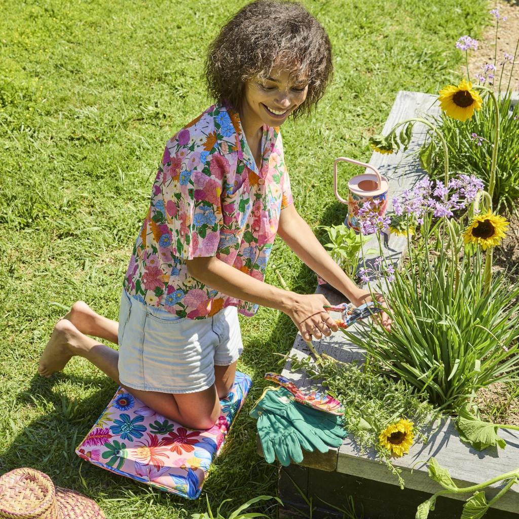 The image shows a gardening set consisting of a pair of secateurs and gloves, placed on a wooden surface. The secateurs have a sleek design with a metallic finish and ergonomic handles, while the gloves are made of a durable material with a floral pattern. Surrounding the tools are various wildflowers in bloom, adding a touch of color and natural beauty to the scene. The overall composition suggests a theme of gardening and nature.