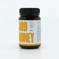 A jar of multifloral honey with a yellow label, featuring the text "100% Multifloral Honey" and "MGO 100+" prominently displayed. The jar is 500g in size and is part of a product line, as indicated by the branding and design elements on the label. The background is plain, emphasizing the product.