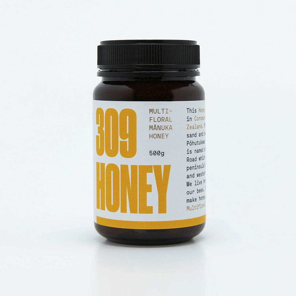 A jar of multifloral honey with a yellow label, featuring the text "100% Multifloral Honey" and "MGO 100+" prominently displayed. The jar is 500g in size and is part of a product line, as indicated by the branding and design elements on the label. The background is plain, emphasizing the product.