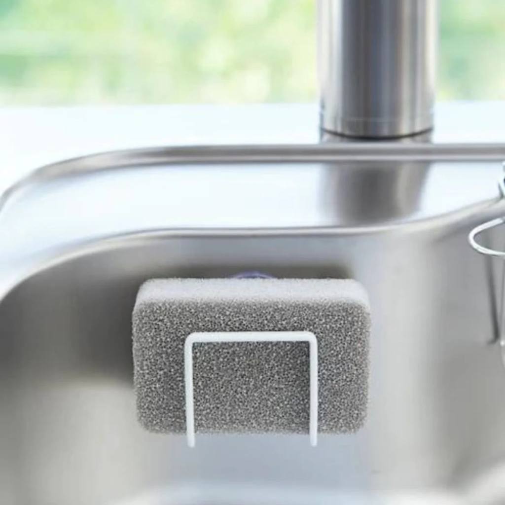 White Yamazaki Tower Sponge Holder with suction cup, attached to a kitchen sink, holding a sponge.