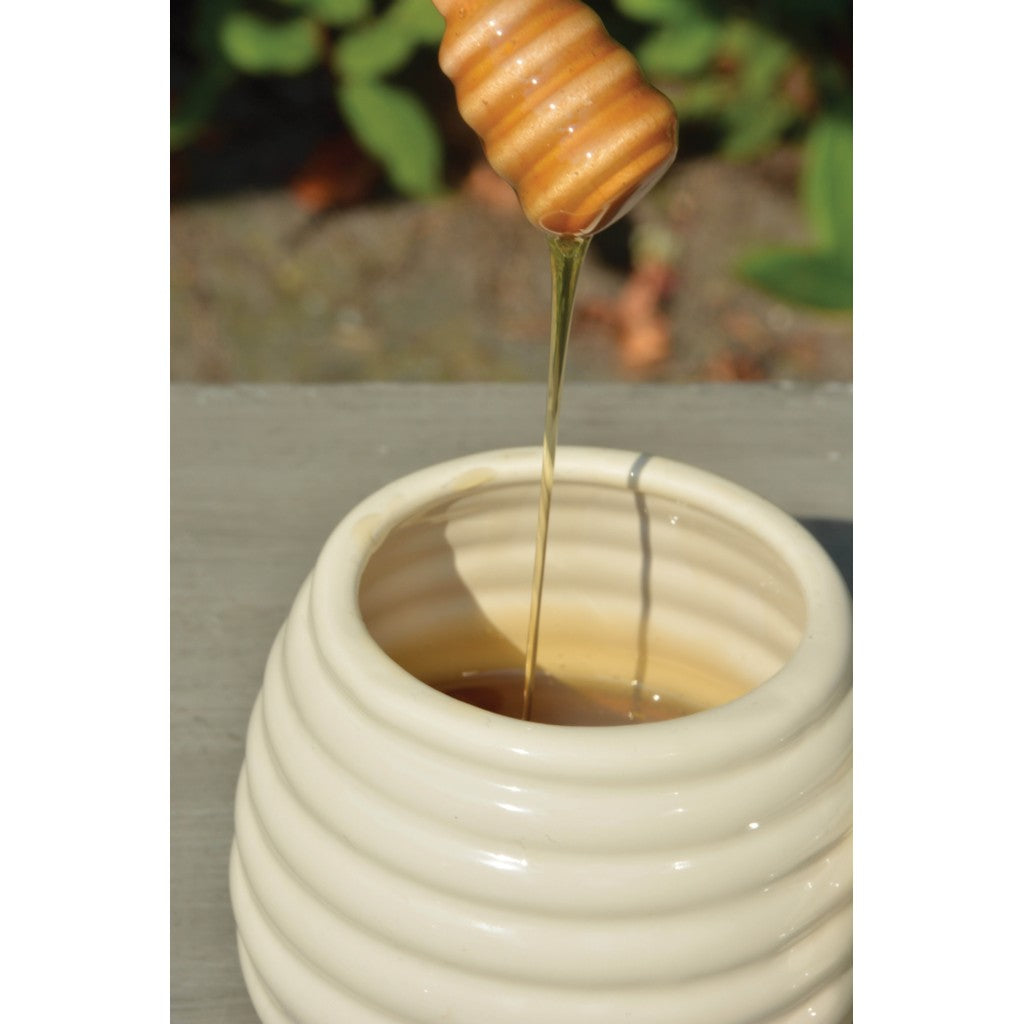 Honey dripping from a dipper into the ceramic honey pot