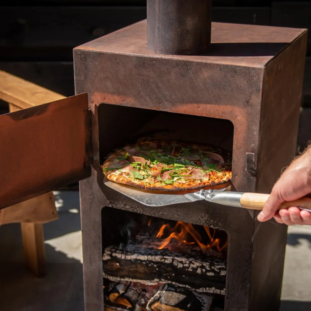 Sliding a pizza into an outdoor pizza oven with the peel