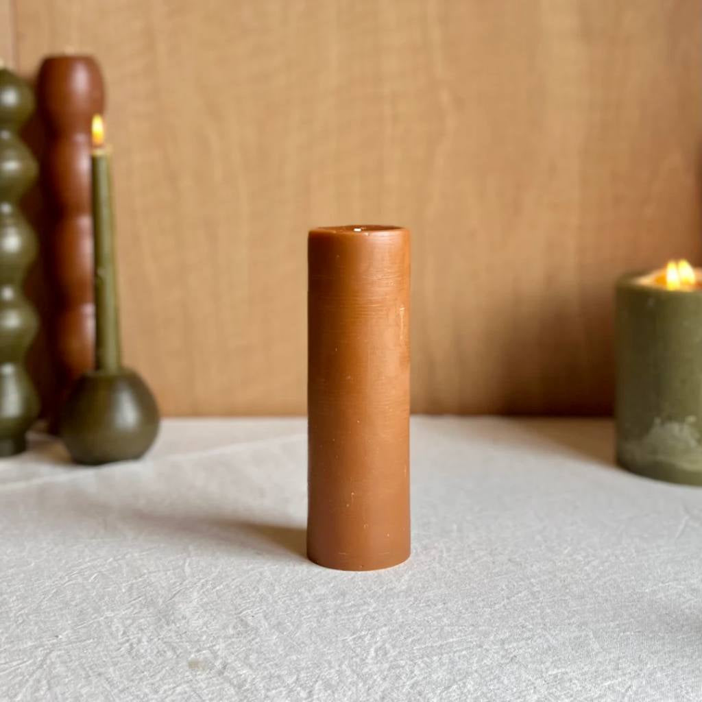 A large amber-colored pillar candle from The Authentic Honey Co., showcasing its smooth surface and rich, warm hue. The candle is set against a plain background, highlighting its elegant and timeless design.