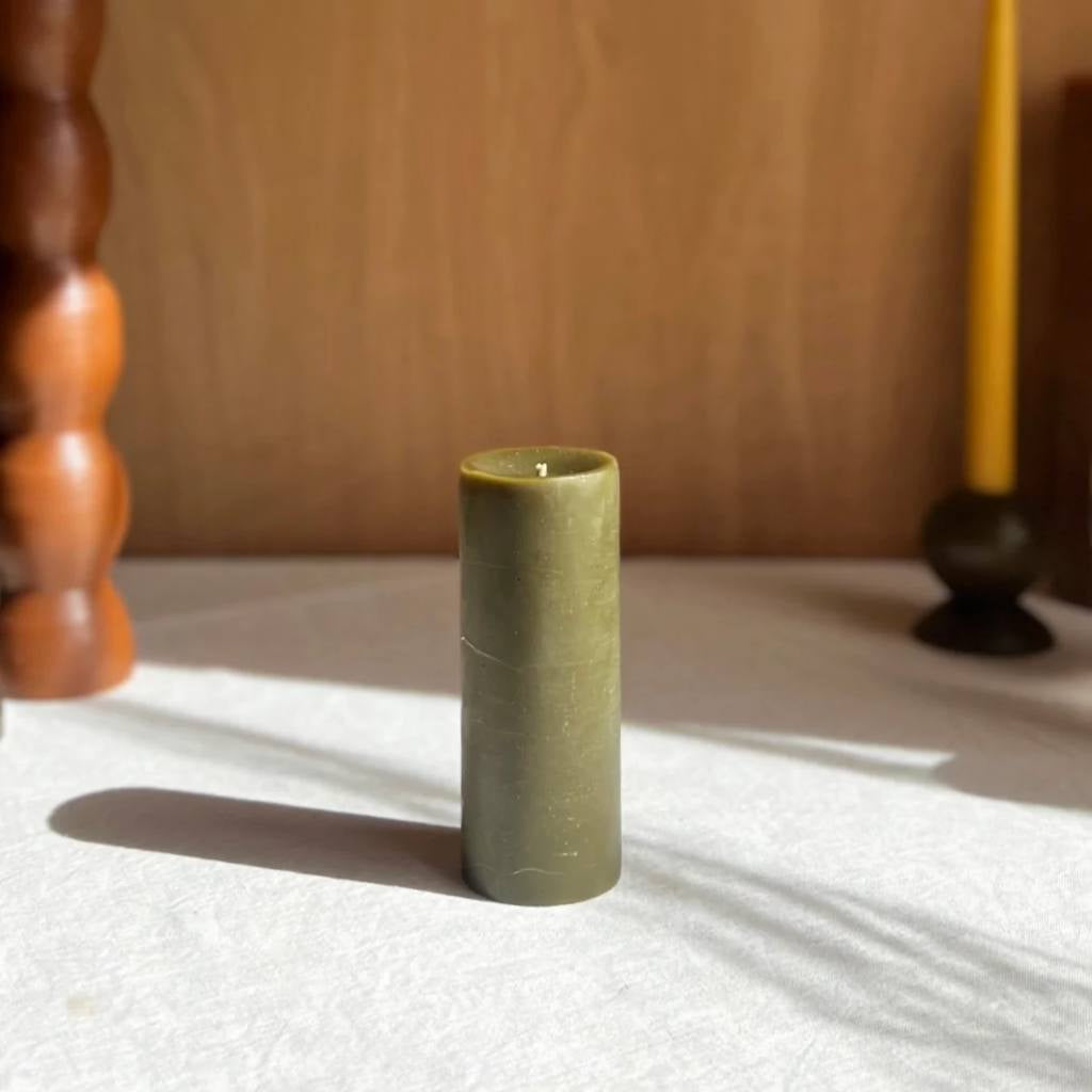 A medium-sized pillar candle in a rich olive color, crafted by The Authentic Honey Co. The candle has a smooth, sleek surface and is set against a plain white background, highlighting its natural hue and elegant design.