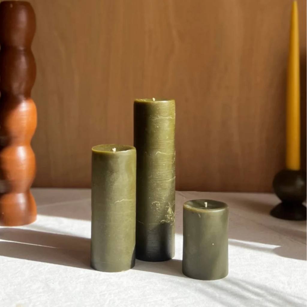 A set of olive green pillar candles from The Authentic Honey Co. displayed on a neutral background. The candles vary in height, showcasing a rustic and natural aesthetic, perfect for home decor or creating a cozy atmosphere.
