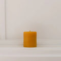 A small, natural beeswax pillar candle from The Authentic Honey Co., showcasing its smooth texture and warm, golden hue. The candle is set against a simple, neutral background, highlighting its handcrafted quality and eco-friendly appeal.
