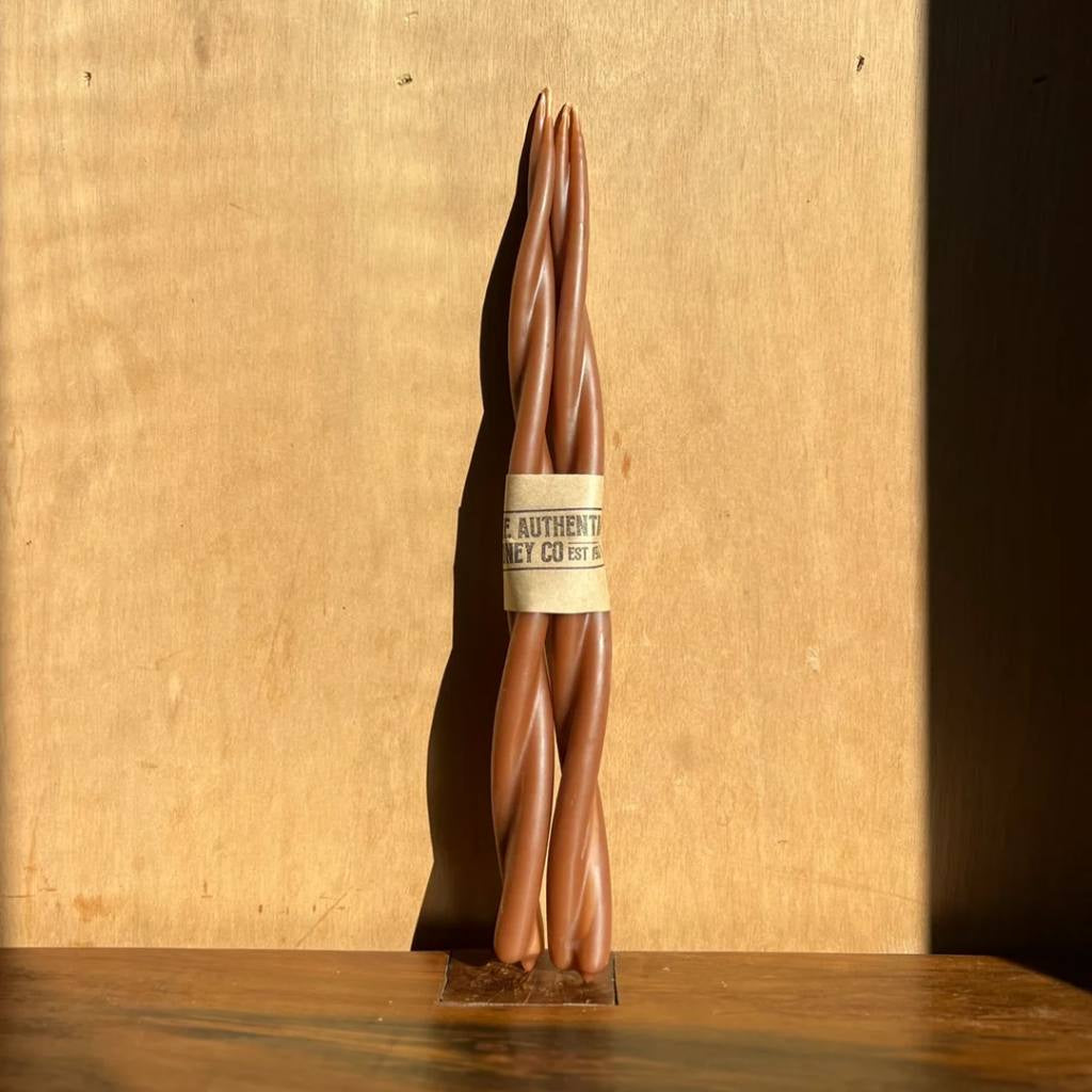 A twisted amber-colored candle from The Authentic Honey Co. displayed against a plain background. The candle features a smooth, spiral design, showcasing its elegant and unique craftsmanship.