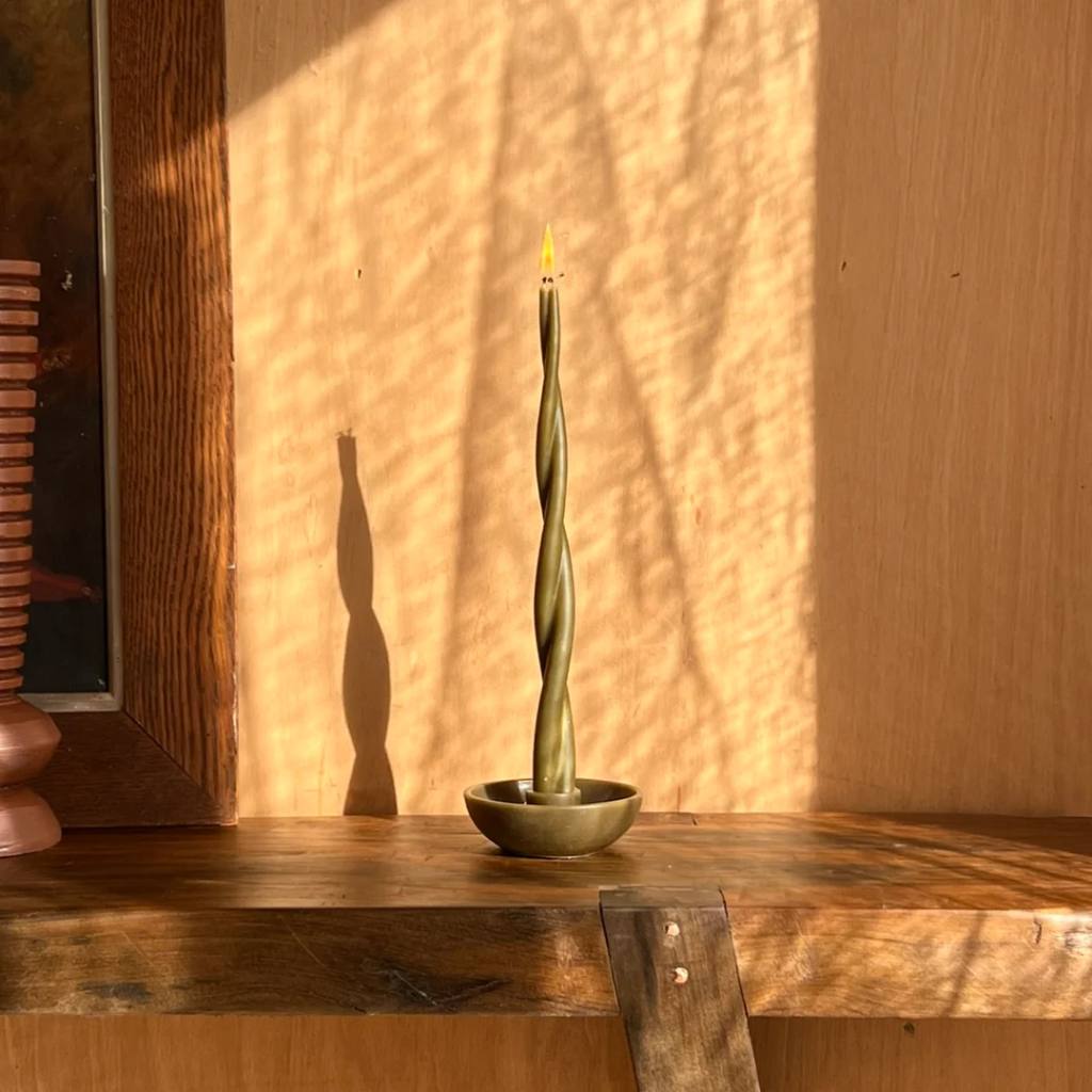 A single olive-colored twist candle from The Authentic Honey Co. displayed against a plain white background. The candle features a unique spiral design, showcasing its elegant and modern aesthetic.